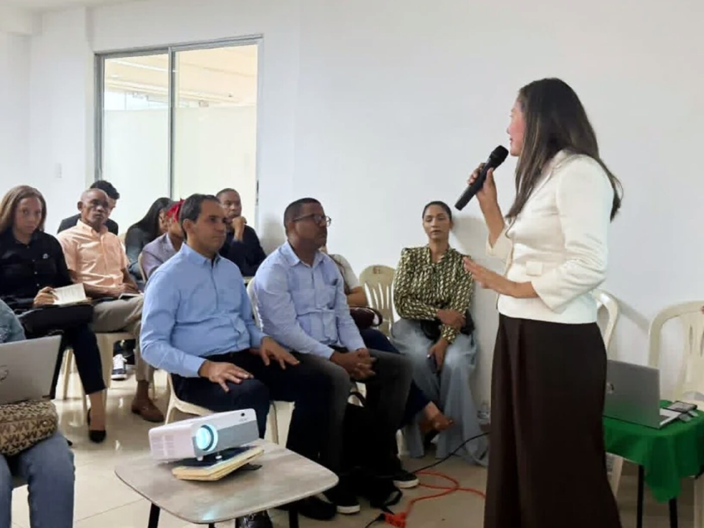 Una de las instructoras habla con micrófono ante los asistentes sentados, durante una dinámica del taller.